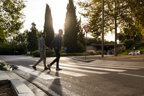 Schwules Paar überquert abends Hand in Hand die Straße, Barcelona, Spanien - AFVF04346