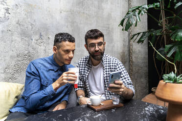 Porträt eines schwulen Paares, das in einem Straßencafé sitzt und auf sein Handy schaut, Barcelona, Spanien - AFVF04348