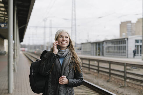 Porträt einer glücklichen jungen Frau, die am Telefon auf den Bahnsteig wartet - AHSF01593