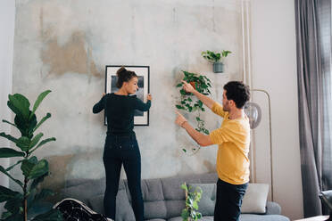 Freund führt Freundin beim Aufhängen eines Bilderrahmens an der Wand in der neuen Wohnung - MASF14763