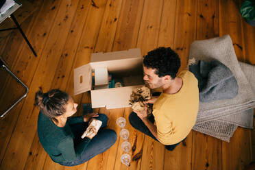 High angle view of couple removing glasses from box in living room at new home - MASF14767