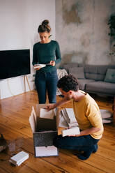 Couple removing novels from box in living room at new home - MASF14770