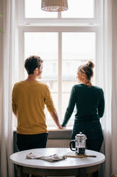 Rückansicht eines romantischen Paares, das am Fenster eines Wohnzimmers steht - MASF14774