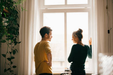 Couple talking while standing by window at home - MASF14775