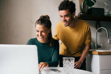 Boyfriend and girlfriend smiling while looking at laptop on table - MASF14782