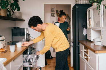 Mid adult man removing cup from drawer below kitchen counter at home - MASF14790