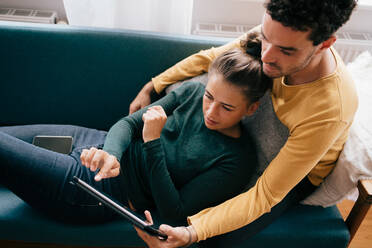 Freund und Freundin benutzen ein digitales Tablet, während sie sich auf dem Sofa zu Hause entspannen - MASF14799