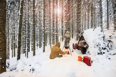 Man preparing tea in winter forest next to a wooden shelter, Salzburg State, Austria - HHF05586