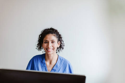 Porträt einer lächelnden, zuversichtlichen Krankenschwester, die an einer weißen Wand im Krankenhaus sitzt, lizenzfreies Stockfoto