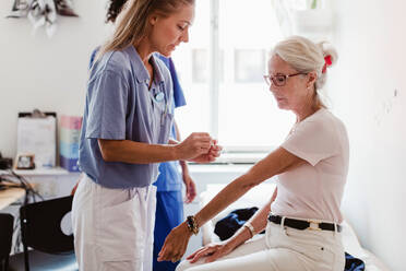Doctor applying bandage on hand of senior woman in medical examination room - MASF14870