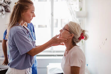 Reife Ärztin, die den Hals eines Patienten im medizinischen Untersuchungsraum untersucht - MASF14872