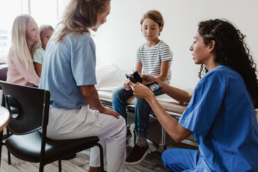 Krankenschwester und Arzt zeigen einem Jungen ein Glaukomgerät, während die Familie in der Klinik sitzt - MASF14889