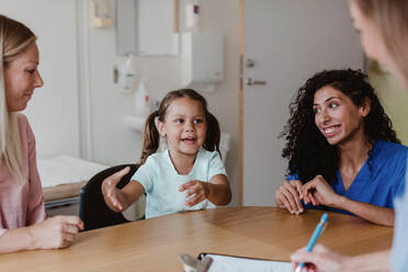 Mädchen im Gespräch mit Arzt, während lächelnde Mutter und Krankenschwester sie im Krankenhaus ansehen - MASF14918