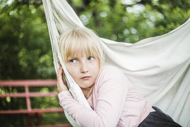 Thoughtful girl looking away while sitting on white swing in garden - MASF14927