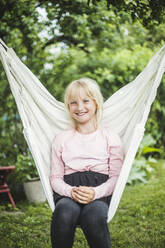 Portrait of smiling girl sitting on white swing in backyard during weekend - MASF14928