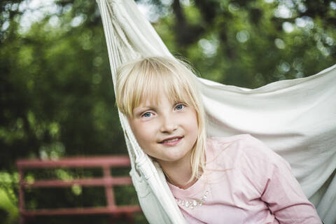 Porträt eines lächelnden Mädchens auf einer weißen Schaukel im Garten, lizenzfreies Stockfoto