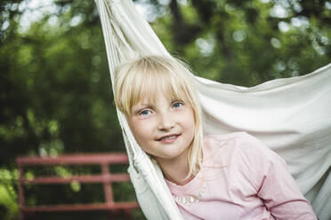 Portrait of smiling girl sitting in white swing in garden - MASF14929