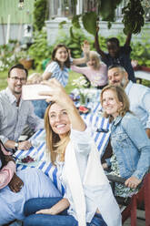 Woman taking selfie with family and friends at dining table in garden party - MASF14937