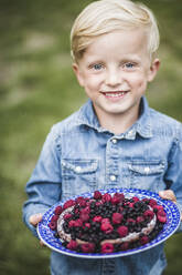 Portrait of smiling boy holding berry tart in garden - MASF14947