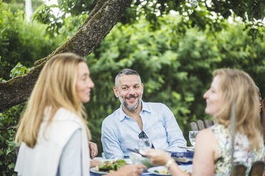 Lächelnder reifer Mann, der seine Freundinnen anschaut, während er eine Gartenparty am Wochenende genießt - MASF14953