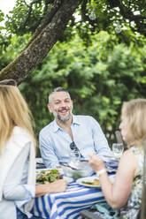 Glücklicher Mann genießt mit Freunden am Esstisch im Garten Party - MASF14955