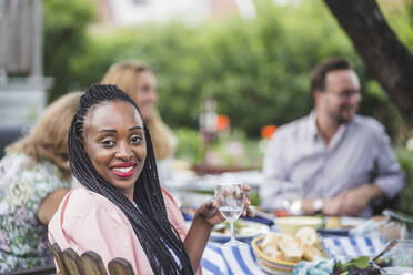 Porträt einer lächelnden Frau, die Wein trinkt, während sie mit Freunden auf einer Gartenparty sitzt - MASF14959