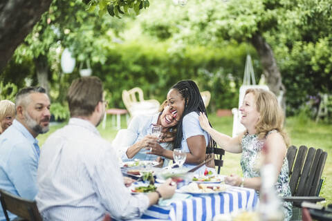 Freunde genießen und haben Spaß beim Sitzen am Esstisch im Garten während des Sommerwochenendes, lizenzfreies Stockfoto