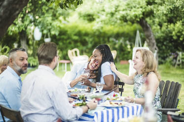 Freunde genießen und haben Spaß beim Sitzen am Esstisch im Garten während des Sommerwochenendes - MASF14961
