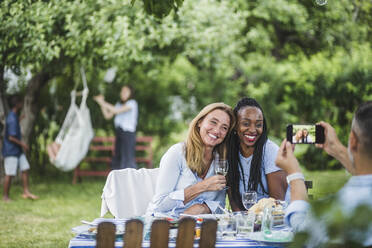 Mann fotografiert Freunde mit Wein durch Handy in Gartenparty - MASF14964