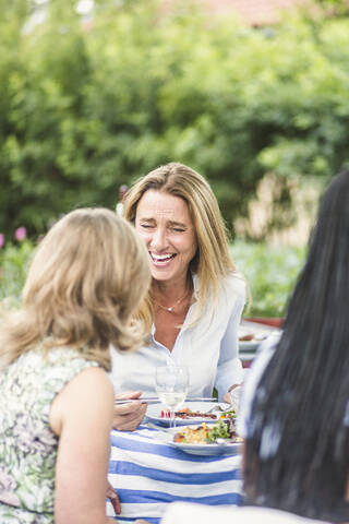 Cheerful female friends enjoying garden party during summer weekend stock photo