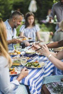 Woman serving food while sitting with friends and family at backyard during weekend party - MASF14972