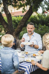 Älterer Mann im Gespräch, während er Kindern auf einer Party einen Teller mit Essen zeigt - MASF14976
