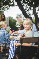 Porträt eines lächelnden Mädchens, das mit Freunden und Familie bei einer Gartenparty am Tisch sitzt - MASF14979