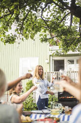 Ältere Frau bereitet Essen auf dem Grill zu, während sie mit Freunden auf einer Gartenparty mit Weingläsern anstößt - MASF14981