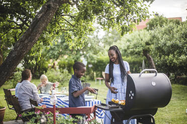 Mutter und Sohn bereiten während einer Wochenendparty im Garten Essen auf dem Grill zu - MASF14992