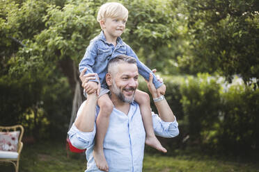 Lächelnder reifer Mann, der seinen Sohn auf der Schulter trägt, während er im Hinterhof Spaß hat - MASF15000