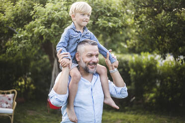 Smiling mature man carrying son on shoulder while having fun in backyard - MASF15000