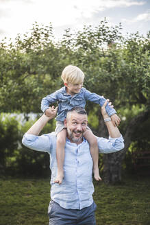 Vater trägt seinen Sohn auf den Schultern im Garten und genießt das Sommerwochenende - MASF15003
