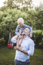 Happy father carrying son on shoulders in backyard - MASF15004