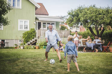 Father playing football with son while friends having fun at table in backyard party - MASF15006