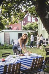 Mature woman arranging food on table in backyard during weekend - MASF15010