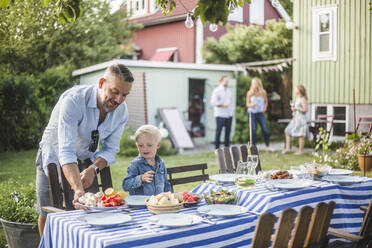 Father talking to son while arranging food plate on table in backyard - MASF15013