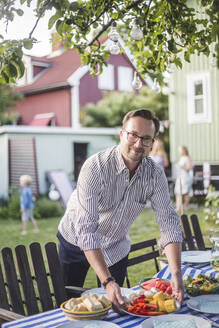 Porträt eines reifen Mannes, der einen Teller auf den Tisch im Hinterhof stellt, während er eine Gartenparty vorbereitet - MASF15016