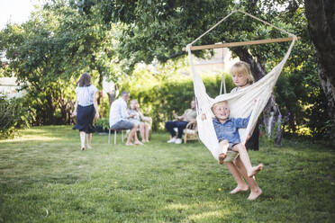 Sister pushing happy boy on swing in backyard - MASF15028