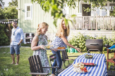 Freundinnen arrangieren Essen auf dem Tisch für ein geselliges Beisammensein im Hinterhof an einem Sommerwochenende - MASF15032