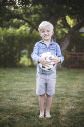 Portrait of cute boy standing while holding football in backyard - MASF15034