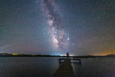 Man standing on dock looking out over harbor at Milky Way - CAVF69462