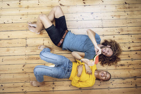 Glückliches junges Paar liegt zu Hause auf dem Boden und teilt sich eine Wassermelone - MCF00529