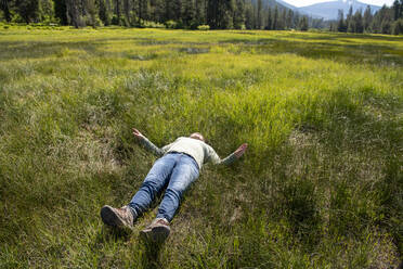 Woman laying in tall green grass of a big green grass valley - CAVF69483