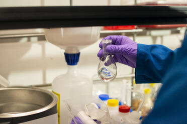 Wissenschaftlerin bei der Vorbereitung der Zugabe einer klaren Flüssigkeit aus einem Florenz-Kolben in einem Labor - CAVF69495